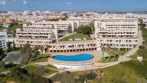 A large hotel with multiple buildings, a central swimming pool, and surrounding greenery.