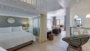 A spacious hotel room with a large bed, a balcony, a dining area, and a kitchen.