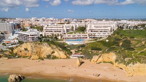 A coastal hotel with multiple buildings, a beach, and rocky cliffs.
