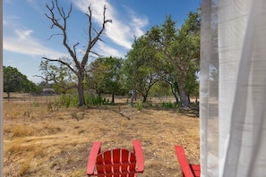 A view of a dry grass field with a red chair in the foreground, a building in the background, and trees with varying foliage. - Blue Moon Tiny Home Pet-Friendly near Old Tunnel (Kendall County)