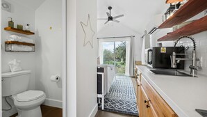 A modern bathroom with a toilet, shower, and sink. There are wooden shelves above the toilet and a star decoration on the wall. - North Star Nook | Tiny Home 6 Min from Old Tunnel (Kendall County)