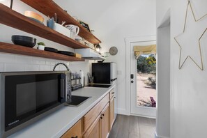 A modern kitchen with white cabinets, a black microwave, and wooden shelves. - North Star Tiny Home 6 Min to Old Tunnel Pets OK (Kendall County)