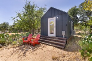 A small, dark-colored cabin with a white door and steps leading up to it. There are two red Adirondack chairs outside. - North Star Tiny Home 6 Min to Old Tunnel Pets OK (Kendall County)