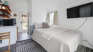 A bedroom with a bed, a desk with a microwave, a TV mounted on the wall, and a patterned rug. - North Star Nook | Tiny Home 6 Min from Old Tunnel (Kendall County)