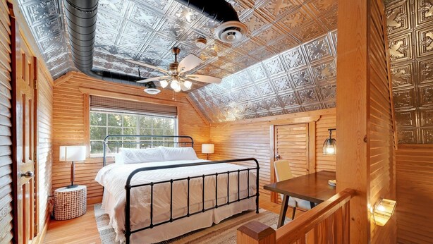 A cozy log cabin bedroom with a bed, a ceiling fan, and a window. - Twilight Ranch- 6 acre ranch w/2tiny homes & cabin (Kendall County)
