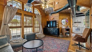 A cozy cabin interior with a large window, a ceiling fan, a television, and a dining area. - Twilight Ranch- 6 acre ranch w/2tiny homes & cabin (Kendall County)