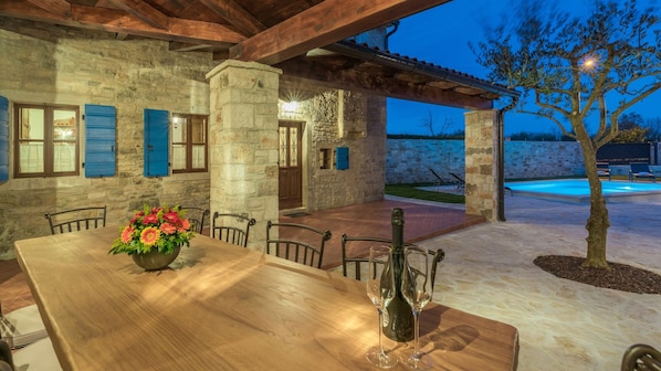 A stone building with a wooden table and chairs, a flower vase, and a wine bottle.