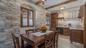 A stone-walled room with a wooden dining table, chairs, and a flower centerpiece.
