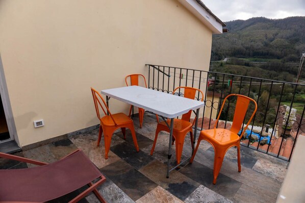 Un balcon avec une table et des chaises, une vue sur un paysage montagneux et un sol carrelé.