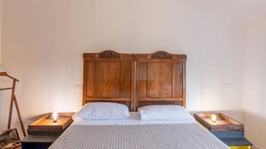 Une chambre à coucher avec une tête de lit en bois, deux oreillers blancs, une couvre-lit à rayures et deux lampes de chevet posées sur des tables de nuit en bois.