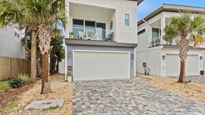 A modern two-story house with a garage, palm trees, and a paved driveway. - Luxury Home 1 Block to Beach with Game Room (Jacksonville Beach)