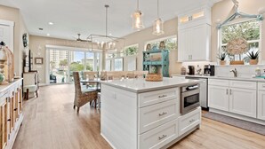 A spacious kitchen with a large island, white cabinetry, pendant lighting, and a view of the outdoors. - Luxury Home 1 Block to Beach with Game Room (Jacksonville Beach)