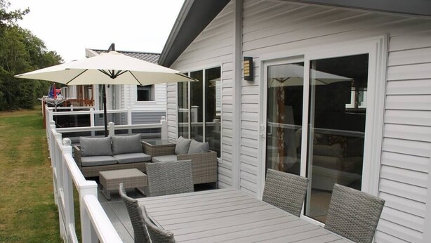 Een overdekt terras met een tafel, stoelen en een bank, plus een grote parasol.