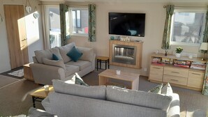 Een gezellige woonkamer met een bank, een salontafel, een open haard en een aan de muur bevestigde televisie.