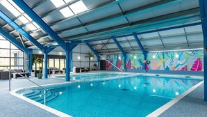 Een binnenzwembad met een blauw betegelde vloer, een kleurrijke muurschildering en een overdekte dakconstructie.