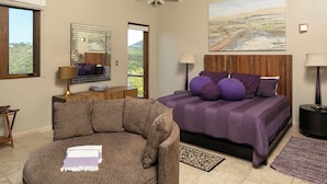 Een slaapkamer met een groot bed, een slaapbank, een houten hoofdeinde, een schilderij en uitzicht op het omliggende landschap.
