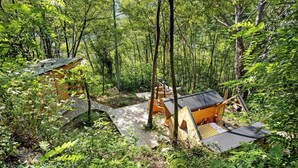Un área boscosa con una pequeña estructura de madera y una construcción más grande tipo cabaña.