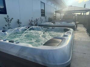 A hot tub area with multiple tubs, a wooden fence, and a building in the background. - Main Residences  (Beenleigh)
