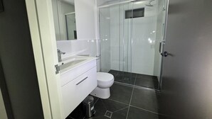 Un bany modern amb plat de dutxa de vidre, un lavabo blanc i un vàter.
