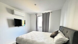 Un dormitori modern amb un llit gran, una televisió de pantalla plana penjada a la paret i una finestra amb cortines.