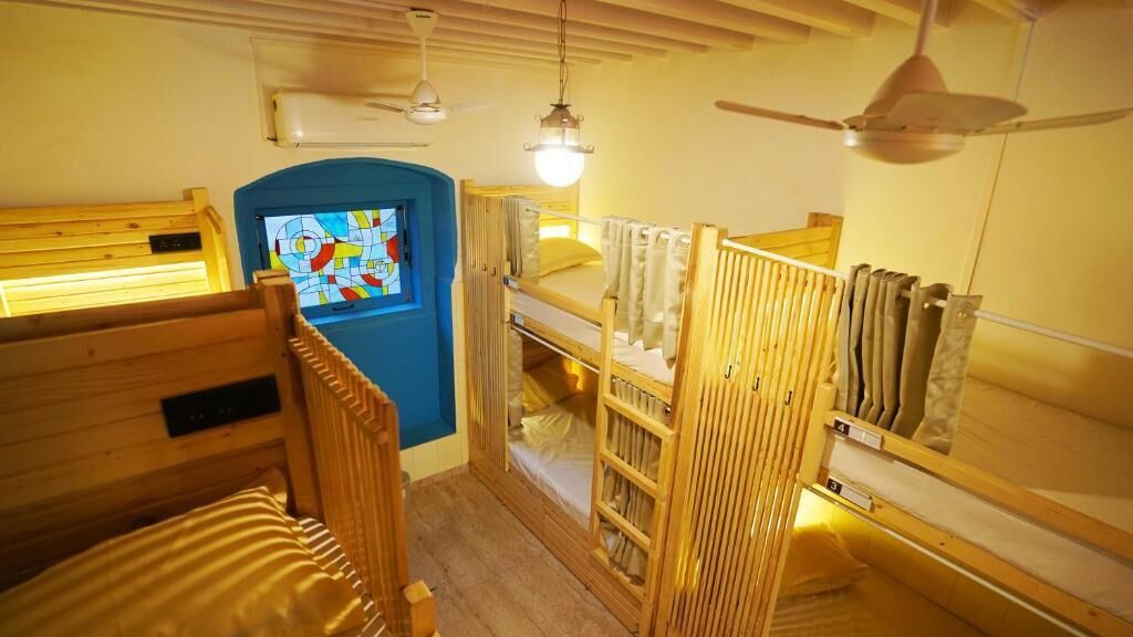 A room with bunk beds, a blue door, a ceiling fan, and a wall-mounted heater.