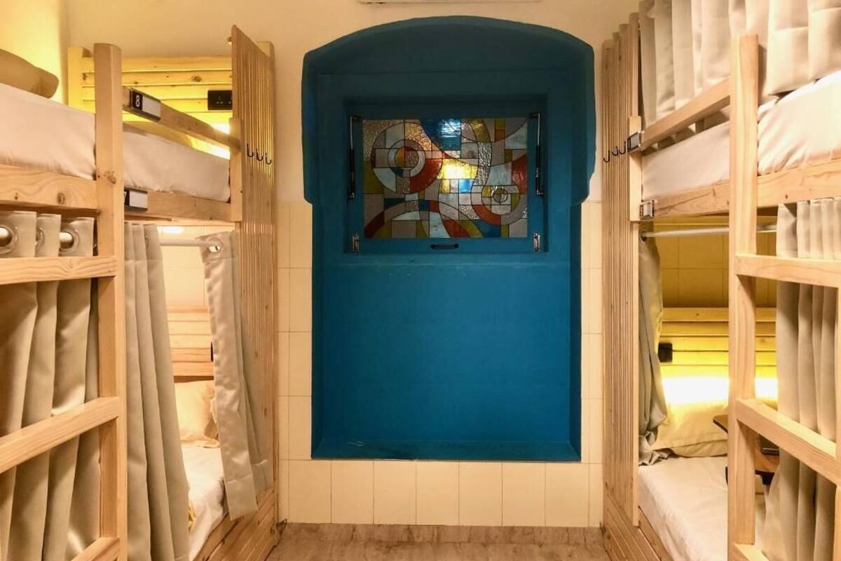 Una habitación con literas, una puerta azul y un ventanal con vidrieras.