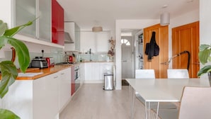 A modern kitchen with white cabinets, a red accent wall, and a dining area with a white table and chairs. - Stunning 1BD Flat w/ Garden Area, Kentish Town! (London)
