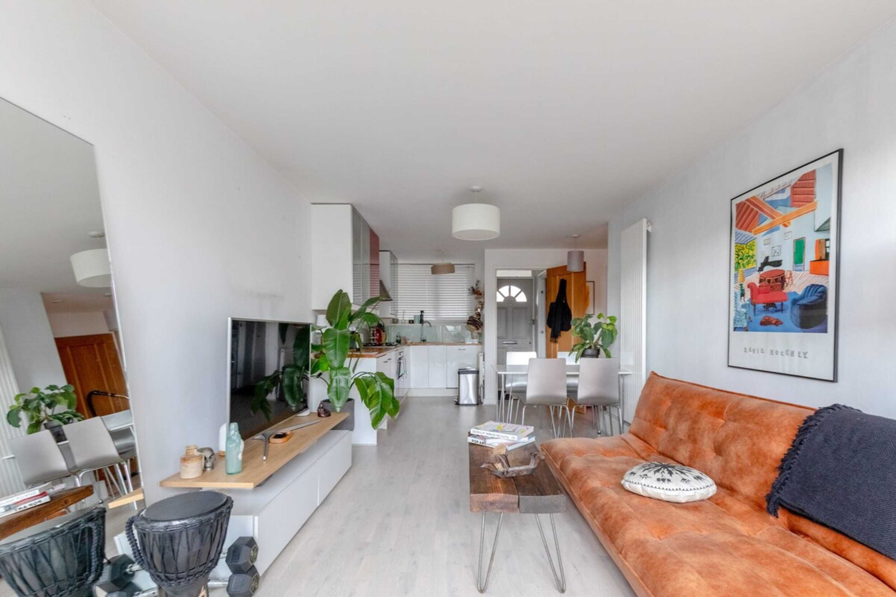 A modern living room with a sofa, coffee table, and a TV. There is a kitchen in the background with white cabinets and a dining area.