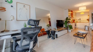 A modern living room with a sofa, a coffee table, and a TV. There is a kitchen area with cabinets and a countertop. - Stunning 1BD Flat w/ Garden Area, Kentish Town! (London)