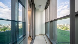 Un balcón estrecho con amplias ventanas que ofrece vistas a un paisaje urbano y campos verdes.