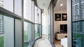 Una habitación de hotel moderna con ventanas amplias, un sendero curvo, una cama, un escritorio y obras de arte en la pared.