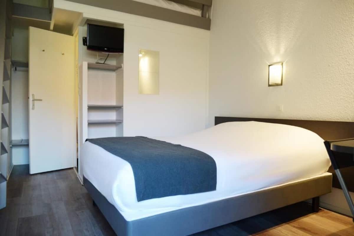 A modern hotel room with a bed, a TV mounted on the wall, and a door leading to a closet.