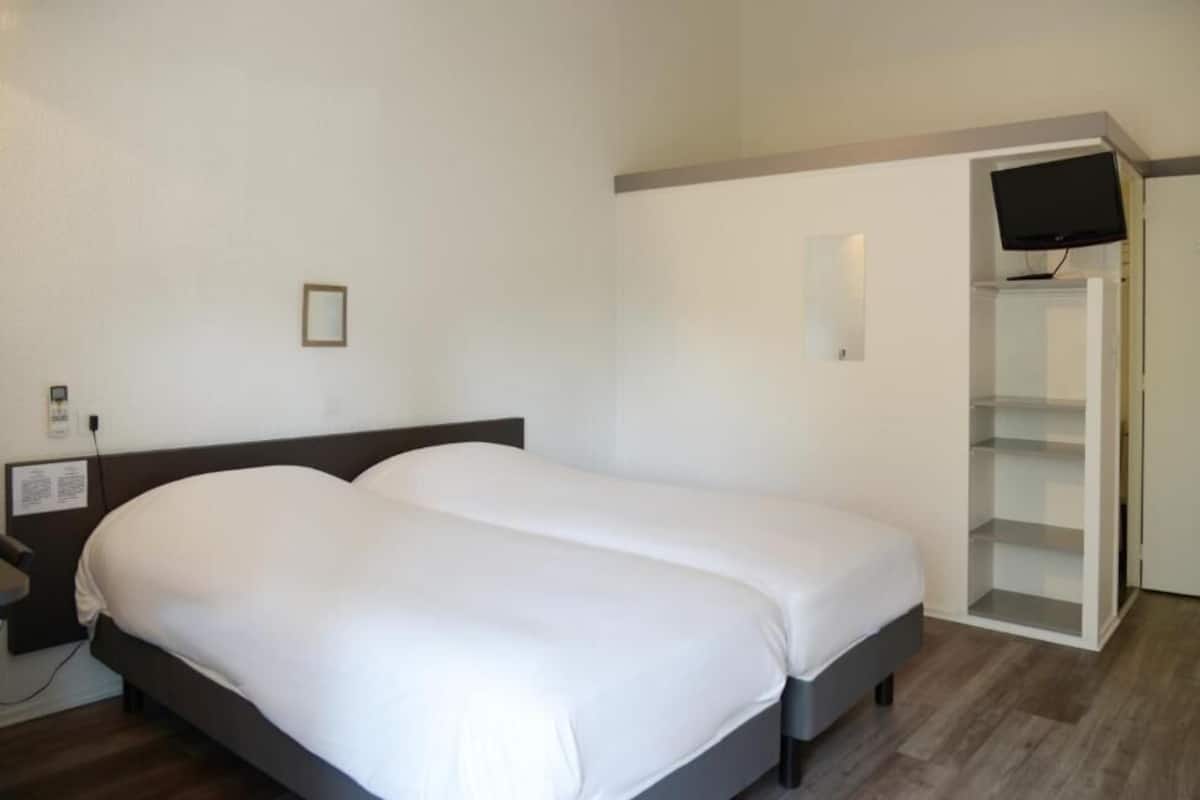 A hotel room with a double bed, a bedside table, a TV mounted on the wall, and a built-in wardrobe.