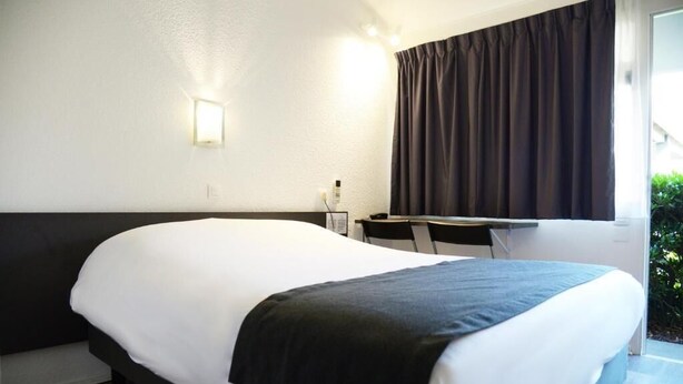 A hotel room with a large bed, a desk, and a window with curtains. - Hôtel Aerel Aéroport Blagnac (Blagnac)