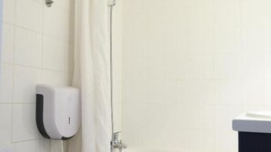 A bathroom with a toilet, a shower with a curtain, a towel hanging on the wall, and a soap dispenser. - Hôtel Aerel Aéroport Blagnac (Blagnac)