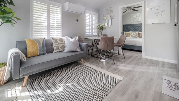 Una sala moderna con un sofá gris, una mesa de comedor con sillas y una cama con cabecera azul.