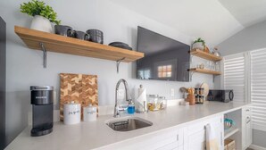 Una cocina moderna con armarios blancos, un lavamanos de acero inoxidable, una cafetera y estantes de madera con utensilios de cocina.