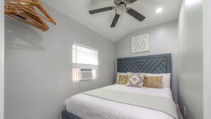 Un dormitorio con cama, ventilador de techo, ventana y una obra de arte en la pared.