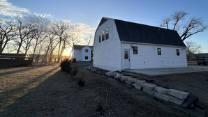 A white single-story house with a dark roof, surrounded by a dirt yard and leafless trees. - Quaint, all new loft apt. located in a quiet country setting, minutes from town. (Fort Pierre)