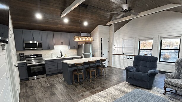 A modern kitchen with dark cabinets, stainless steel appliances, and a central island with bar stools. - Quaint, all new loft apt. located in a quiet country setting, minutes from town. (Fort Pierre)