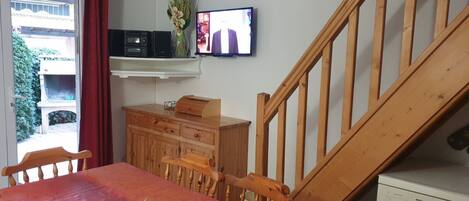 A dining area with a wooden table, chairs, a red tablecloth, a television, a wooden cabinet, and a staircase.
