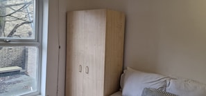 Enjoy a serene view from this corner room, featuring a wardrobe with two doors and a sofa with a pillow and cushion.