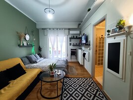 A compact living space with a sofa, a coffee table, a bed, a TV, and a kitchen area.