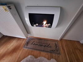 A modern fireplace with a fire burning, a radiator to the left, and a doormat with the phrase "happiness is homemade" in front.