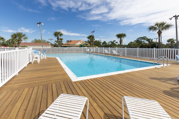 Una terraza de madera con piscina, barandillas blancas y sillas de descanso.