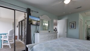 A bedroom with a large bed, a TV mounted on the wall, a dresser, and a sliding glass door leading to an outdoor area with chairs and a table. - Pal306- Super Cute! Awesome Pool, & Beach Gear Included! Location X3! (Orange Beach)