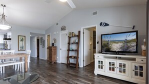 A spacious living room with a wooden floor, a glass coffee table, a television, and a bookshelf. - Pal306- Super Cute! Awesome Pool, & Beach Gear Included! Location X3! (Orange Beach)