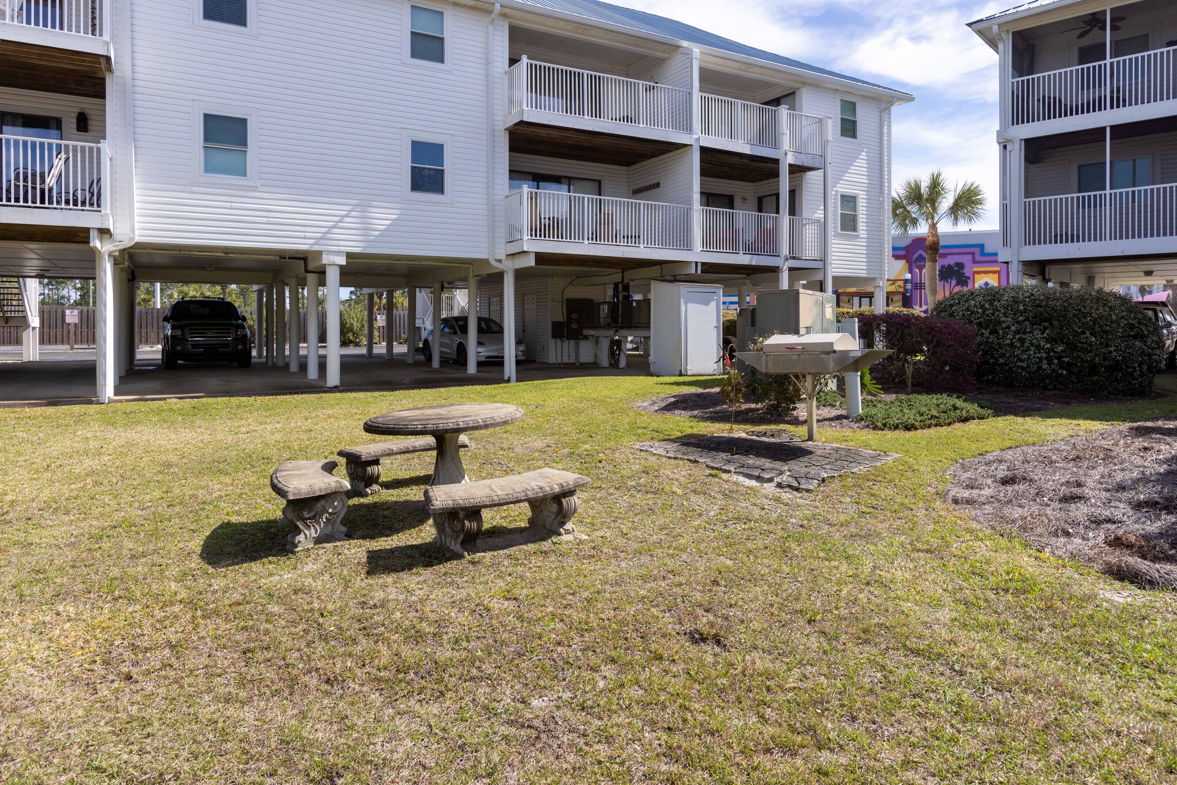 A multi-story building with balconies, a covered parking area, and a small outdoor seating area with a table and benches.