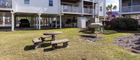 A multi-story building with balconies, a covered parking area, and a small outdoor seating area with a table and benches.