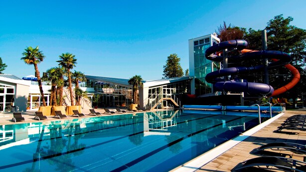 Une piscine à l’eau d’un bleu cristallin, entourée de chaises longues et de palmiers.